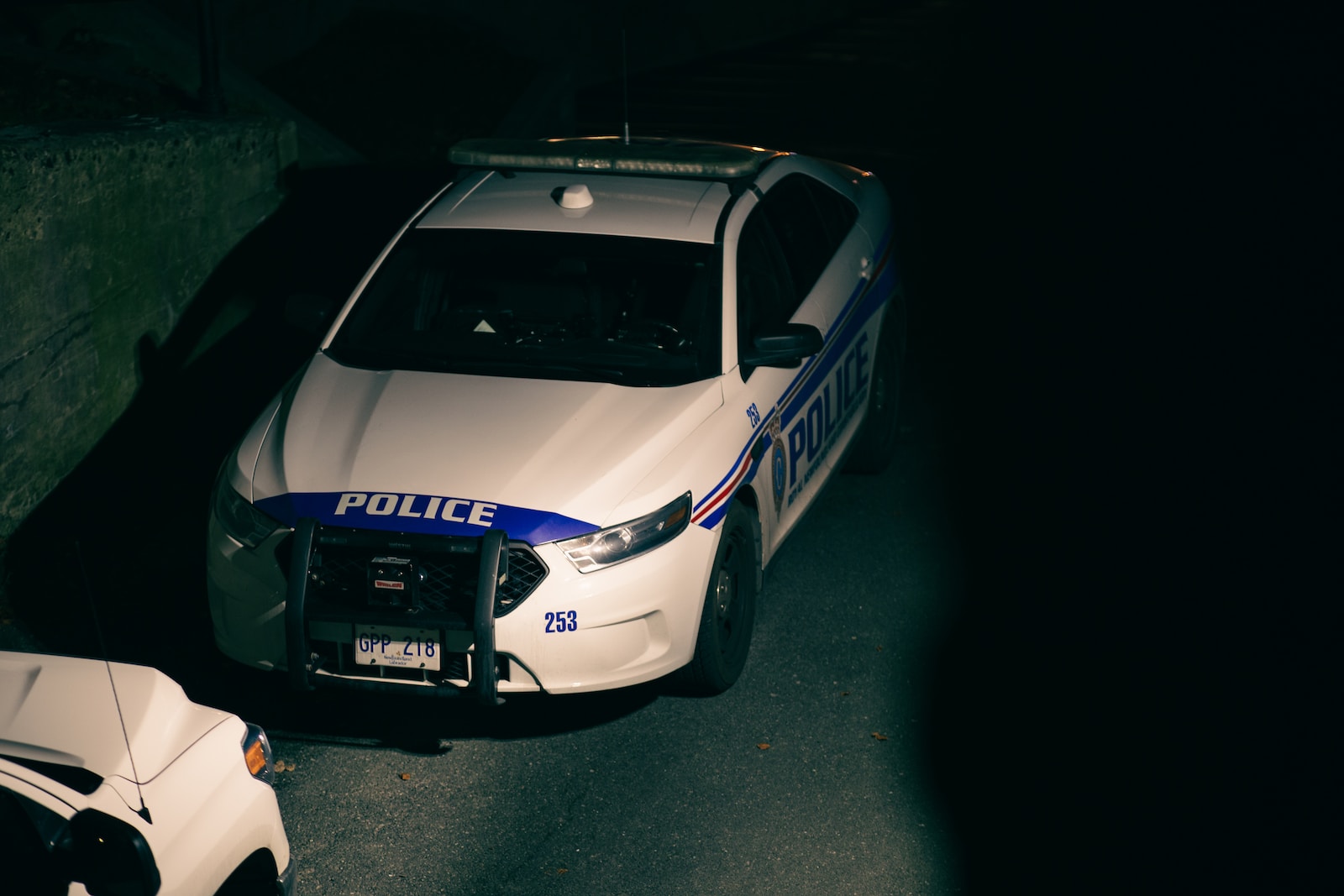 Night time scene of white police car with blue writing.