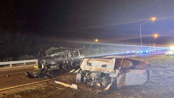 Night time highway scene shows two vehicles, one white, one black, both wrecked and mangled beyond recognition of make or model.