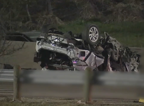 Nighttime edge of freeway scene. A white vehicle is mangled and shown flipped onto its roof.