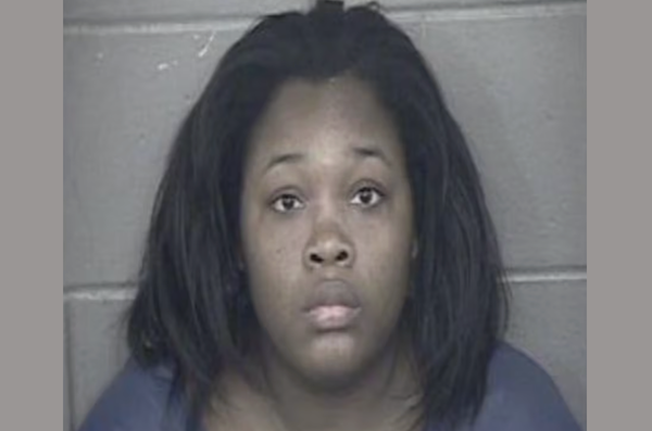 A woman with long dark brown hair wears a muted purple shirt as she looks plaintively at the camera during her mugshot.