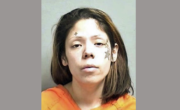A woman in an orange shirt barely opens her eyes during her mugshot. She has shoulder length medium brown hair and a large star tattoo on her cheek along with other small facial tattoos.