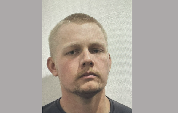 A white man with buzz cut blond hair and a blond mustache and goatee stares at the camera during his mugshot with a somewhat angry expression.