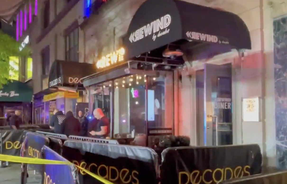 Exterior of a nightclub called Decades. Yellow crime scene tape cordons off the entrance with its black awnings and railings.