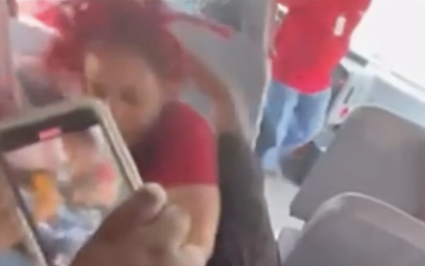Blurry cell phone footage of a woman grabbing a child from a school bus seat while another student films with a mobile phone and the bus driver stands up from his seat.