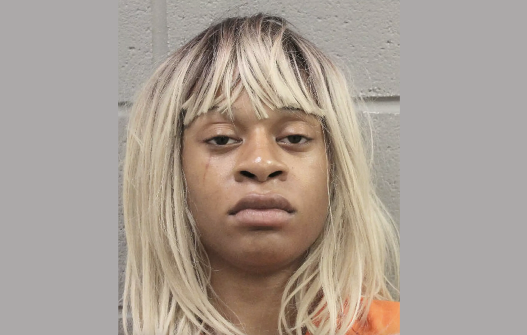 A young woman with long blonde hair looks scornful during her mugshot. She wears an orange shirt.