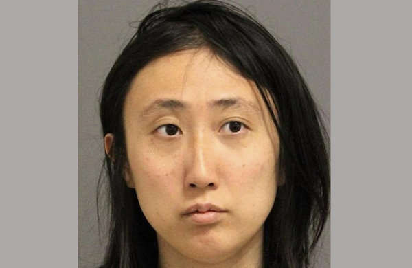 A young woman with long dark brown hair parted down the middle looks sad and disheveled during her mugshot.