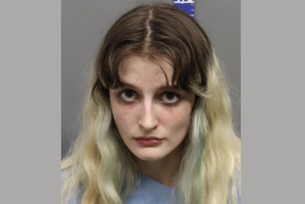 A young white woman with dark brown hair died light blonde and blue on the ends wears heavy eye-makeup and looks angrily up at the camera during her mugshot.