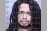 Mugshot of a man with long dreadlocks and a short beard, wearing an orange shirt, with a watermark overlay from a sheriff’s office.