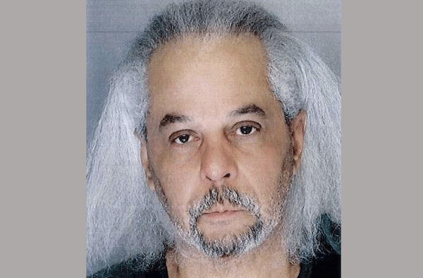 Mugshot of an older man with gray, shoulder-length hair and a beard, set against a neutral background.