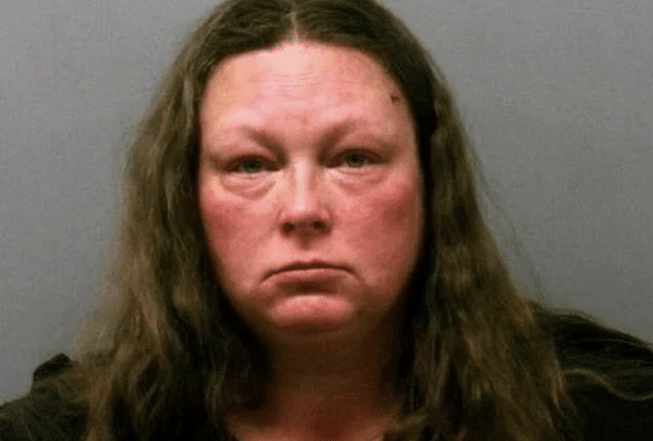 A woman with long brown hair and a serious expression is photographed against a plain gray background.