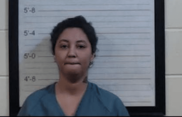 Mugshot-style photo of a woman in a blue jail uniform standing in front of a height chart.