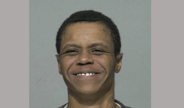Close-up mugshot of a smiling person with short dark hair against a plain gray background.