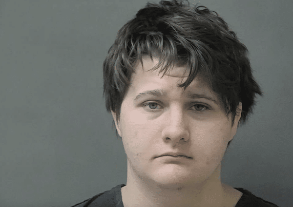 Booking photo of a young person with short dark hair facing the camera against a plain gray background.