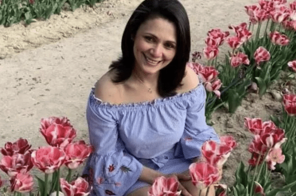 Smiling woman sitting in a flower garden surrounded by pink tulips, wearing an off-the-shoulder blue blouse.