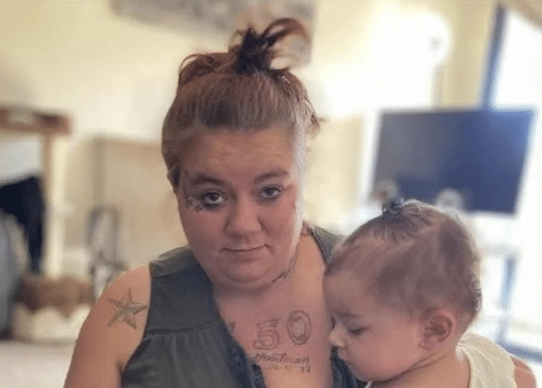 Woman with red hair in a bun holds a small child indoors while looking at the camera.