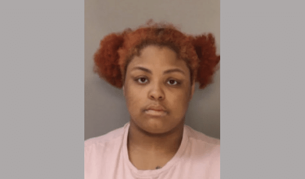 Mugshot-style photo of a young woman with reddish-orange hair against a gray background.