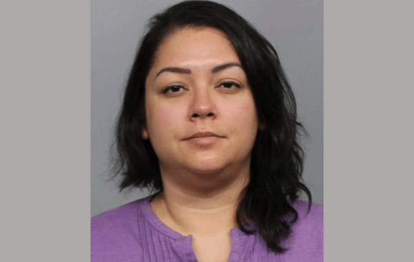 Head-and-shoulders portrait of a woman with dark shoulder-length hair wearing a purple shirt against a plain gray background.