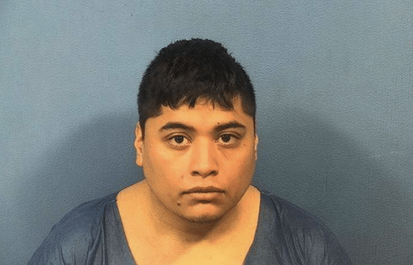 Front-facing portrait of a person with short dark hair against a plain blue wall.