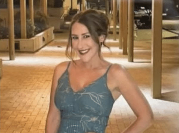 Smiling woman in a blue patterned spaghetti-strap dress poses outdoors at night under warm lights.