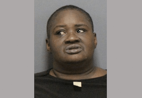 Close-up booking photo of a person in a dark shirt against a plain gray background, looking off to the side.