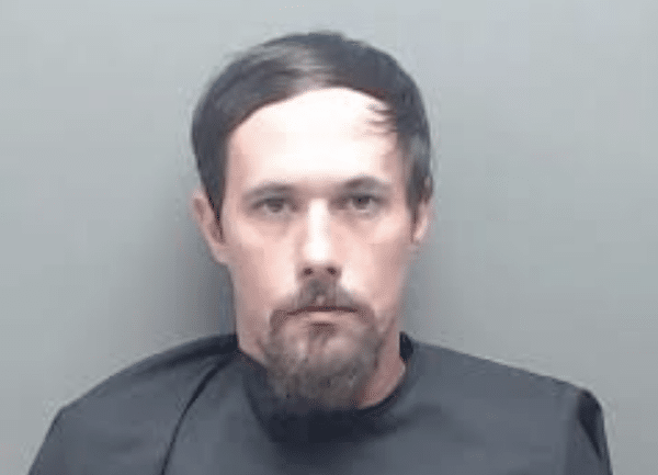 A man with short dark hair and a goatee faces the camera against a plain gray background.