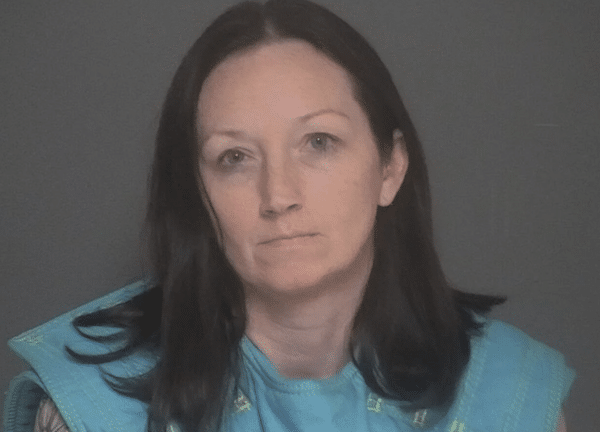 Blurry mugshot-style image of a man with short twisted dreadlocks and a beard wearing a blue jail uniform against a gray block wall.