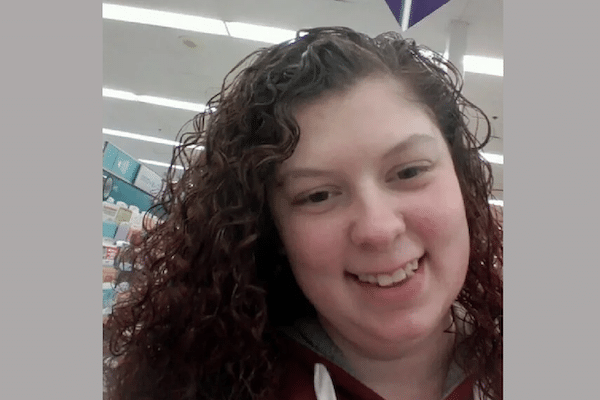 A smiling person with curly hair takes a selfie inside a brightly lit retail store.