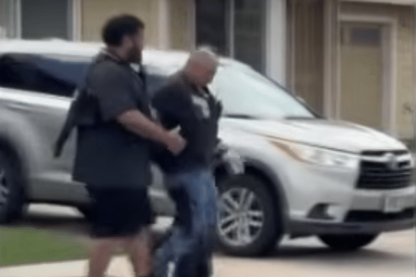 Two men walk on a residential lawn beside a silver SUV, with one appearing to escort the other near an apartment building.
