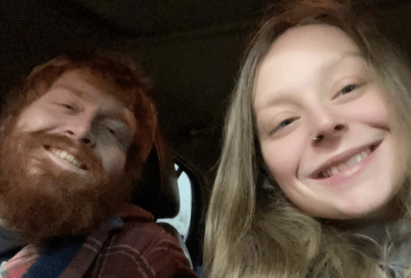 Selfie of a smiling bearded man and a smiling young woman sitting together inside a vehicle.