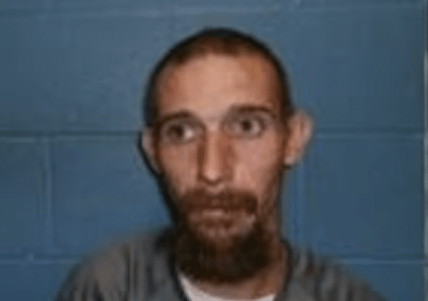 Blurry close-up image of a man with a beard standing against a blue wall.