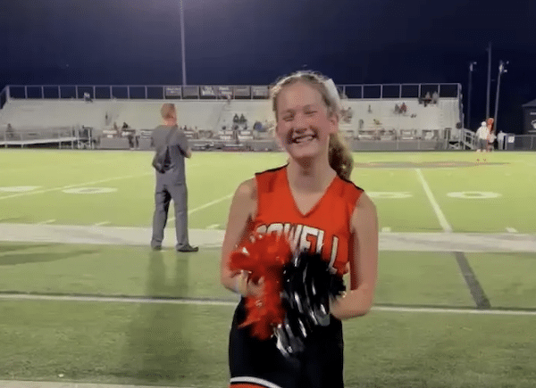 Photo of a smiling cheerleader holding red and black pom-poms on a football field at night.