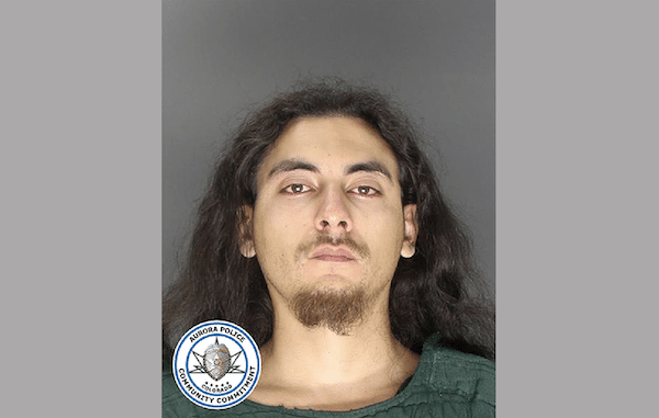 Booking-style photo of a man with long dark hair and facial hair against a gray background.