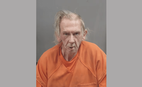 Mugshot-style photo of an older man wearing an orange jail uniform against a gray background.