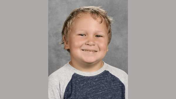 Smiling young child poses for a school-style portrait against a gray background.