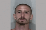 Mugshot-style portrait of a man with a shaved head and trimmed beard against a plain wall.