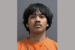 Mugshot-style portrait of a young man with dark shaggy hair wearing an orange jail uniform.