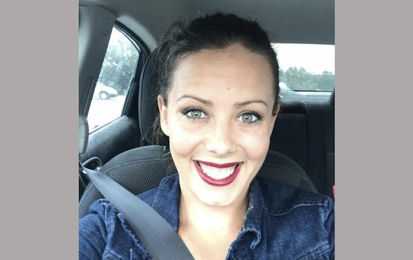 Smiling woman takes a selfie while seated in a car wearing a seat belt.