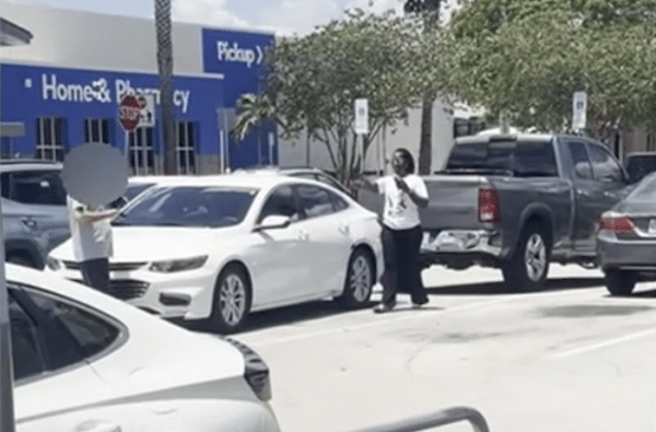 Parking lot scene showing two people near several parked cars, with one person’s face obscured.