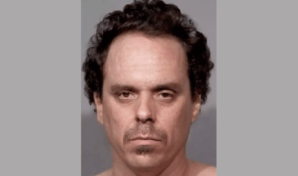 Front-facing booking-style portrait of a man with short curly dark hair, light facial hair and a neutral expression.
