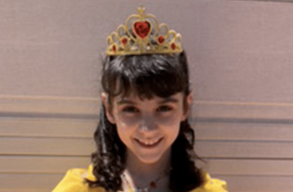 Smiling young girl with dark hair wearing a gold-and-red tiara and a bright yellow costume.