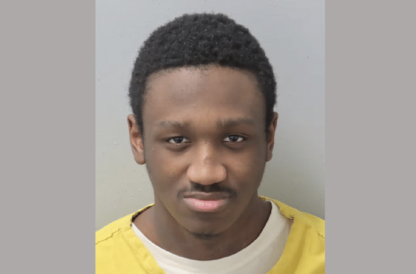 Mugshot-style photograph of a young Black man with short hair wearing a yellow jail uniform against a plain gray background.